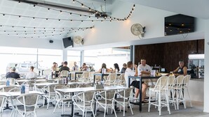 Un vaste espace intérieur aménagé en salle à manger, avec de nombreuses tables et chaises, un comptoir de bar et un grand écran fixé au mur.