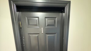 A dark brown door with a keypad lock, positioned in a hallway with light-colored walls and wooden flooring. - Perfect place to stay for events at the Lazy E (Guthrie)
