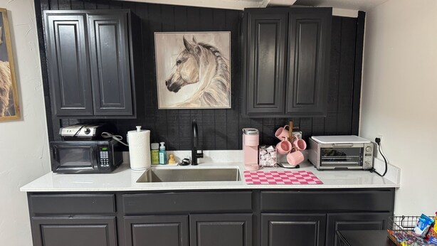 A kitchen with dark cabinets, a microwave, a toaster, a sink, and a countertop with various items. - Perfect place to stay for events at the Lazy E (Guthrie)