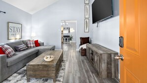 A modern living room with a grey sofa, wooden coffee table, and a flat-screen TV mounted on the wall. - Current Bungalow 5 Beds Pro Turnkey MP Getaways (Clarksville)