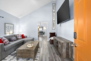 Een moderne woonkamer met een grijze bank, een houten salontafel en een flatscreen televisie aan de muur.
