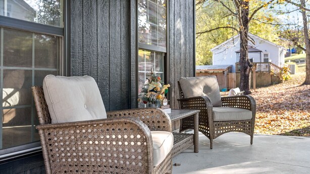 A wicker chair and table set on a porch with a view of a house and trees. - Current Bungalow 5 Beds Pro Turnkey MP Getaways (Clarksville)