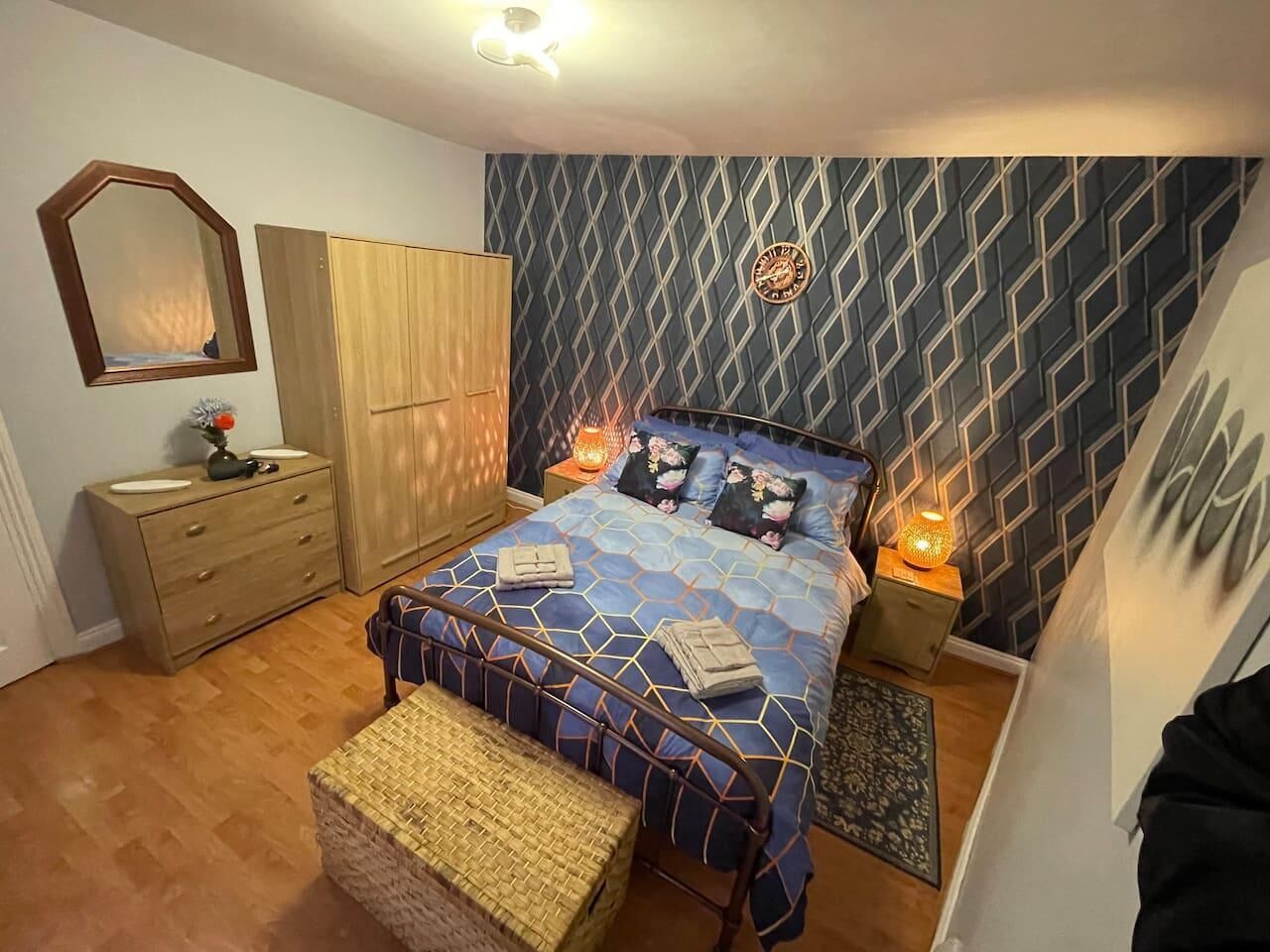 A bedroom with a bed, wooden wardrobe, dresser, and a mirror.