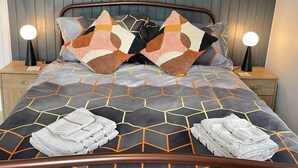 A neatly made bed with a geometric patterned bedspread, two decorative pillows, and two folded towels on the bed. - Impeccable 4-Bed Home Away From Home in Swindon (Swindon)