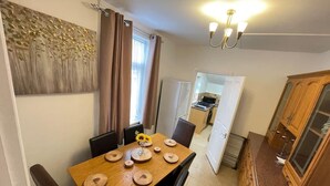 A dining area with a wooden table set for four, a vase with flowers, and a kitchen in the background. - Impeccable 4-Bed Home Away From Home in Swindon (Swindon)