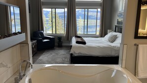 Ein modernes Schlafzimmer mit einer großzügigen Badewanne, einem Bett mit weißen Leinen, einem Sessel und Bergblick durch große Fenster.