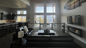 Ein modernes Wohnzimmer mit einer schwarzen Ledersofa, einem Couchtisch und Blick auf Berge durch große Fenster.