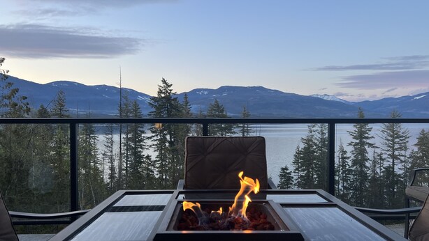 Ein Balkon mit Glastisch, Feuerstelle und Blick auf Berge und Bäume.