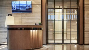 A reception desk with a television mounted on the wall, a small plant on the desk, and a glass door entrance. - HuaMan Hotel DongGuan TangXia (Dongguan)