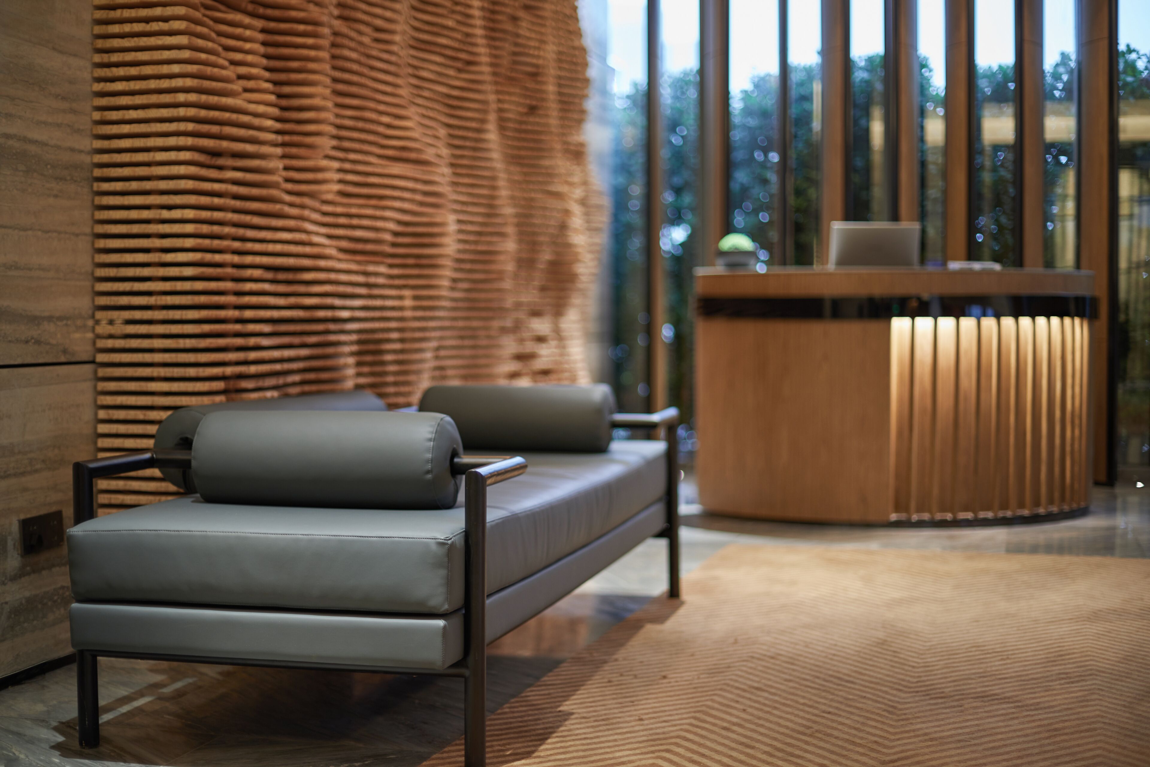 A modern interior with a sofa, a wooden reception desk, and a patterned wall.