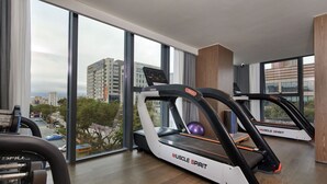 A modern gym with treadmills, a rowing machine, and a large window with a city view. - HuaMan Hotel DongGuan TangXia (Dongguan)