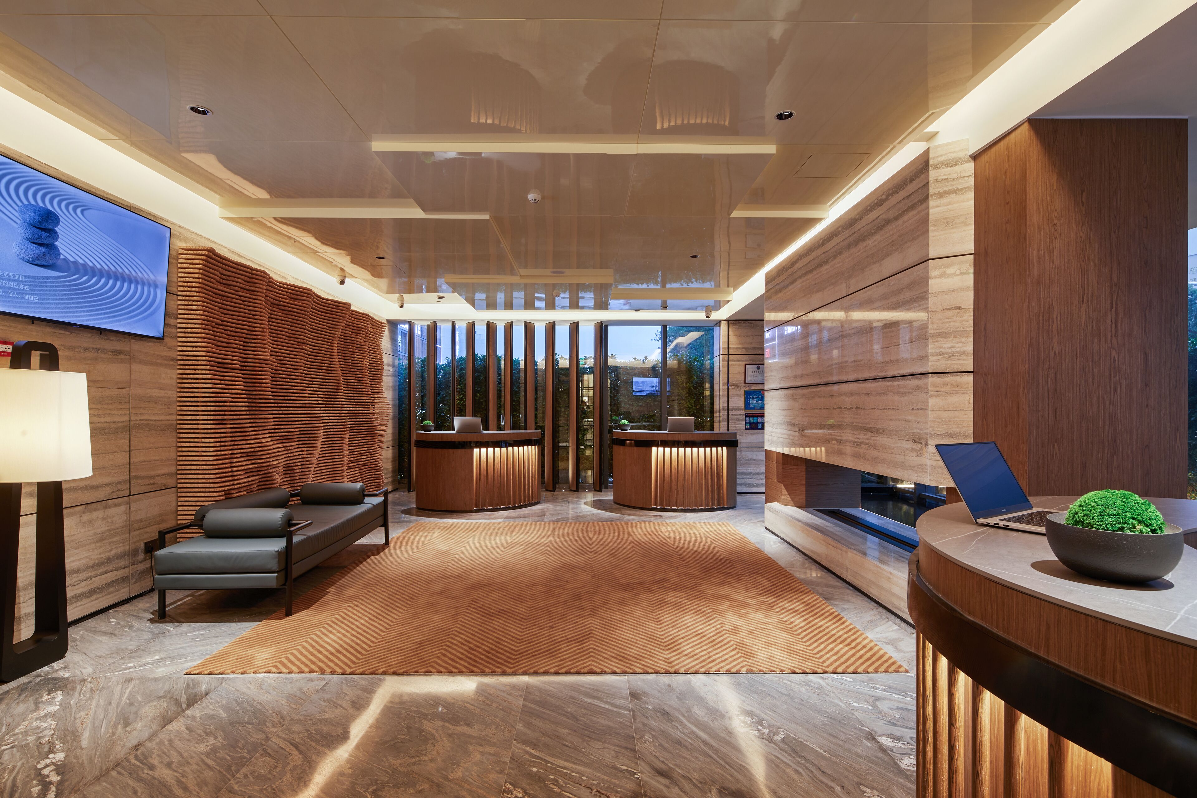 A modern lobby with a reception desk, seating area, and a large TV screen.