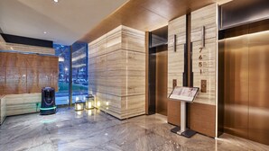A modern lobby with a marble floor, wooden paneling, and two elevators. - HuaMan Hotel DongGuan TangXia (Dongguan)