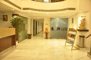 A hotel lobby with a reception desk, a plant, a bulletin board, and a 'No Smoking' sign. - Arch Plaza - Near Yashobhoomi Dwarka (New Delhi)