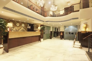 A hotel reception area with a marble floor, a reception desk, a staircase, and a chandelier.