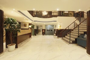 Eine geräumige Lobby mit Marmorboden, einem Empfangsbereich, einer Treppe und einer großen Pflanze.