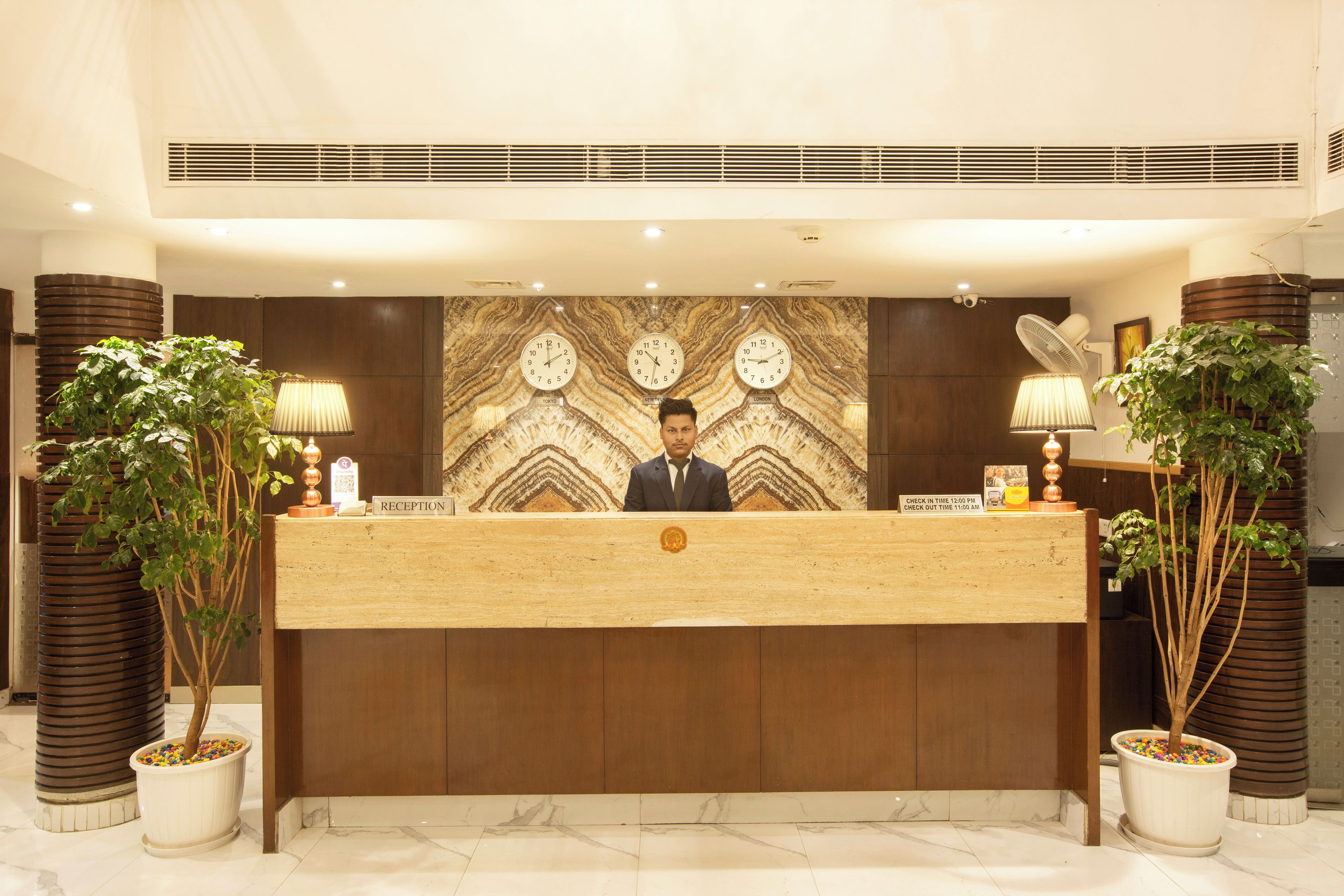 A reception desk with a receptionist, a clock, and two potted plants.