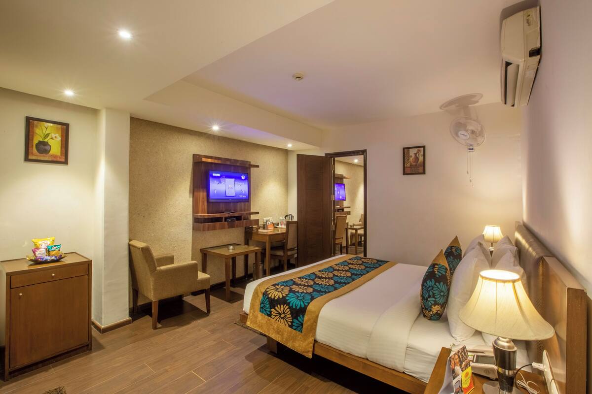 Een hotelkamer met een bed, bedlamp, bureau, stoel, televisie en een klein kastje.