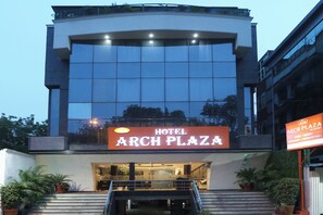 Un hôtel à la façade moderne, avec une enseigne bien visible indiquant « ARCH PLAZA HOTEL », et un escalier menant à l’entrée.
