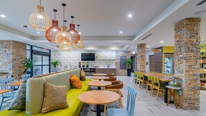 Ein modernes Restaurant mit einer grünen Couch, runden Tischen und hängenden Pendelleuchten.