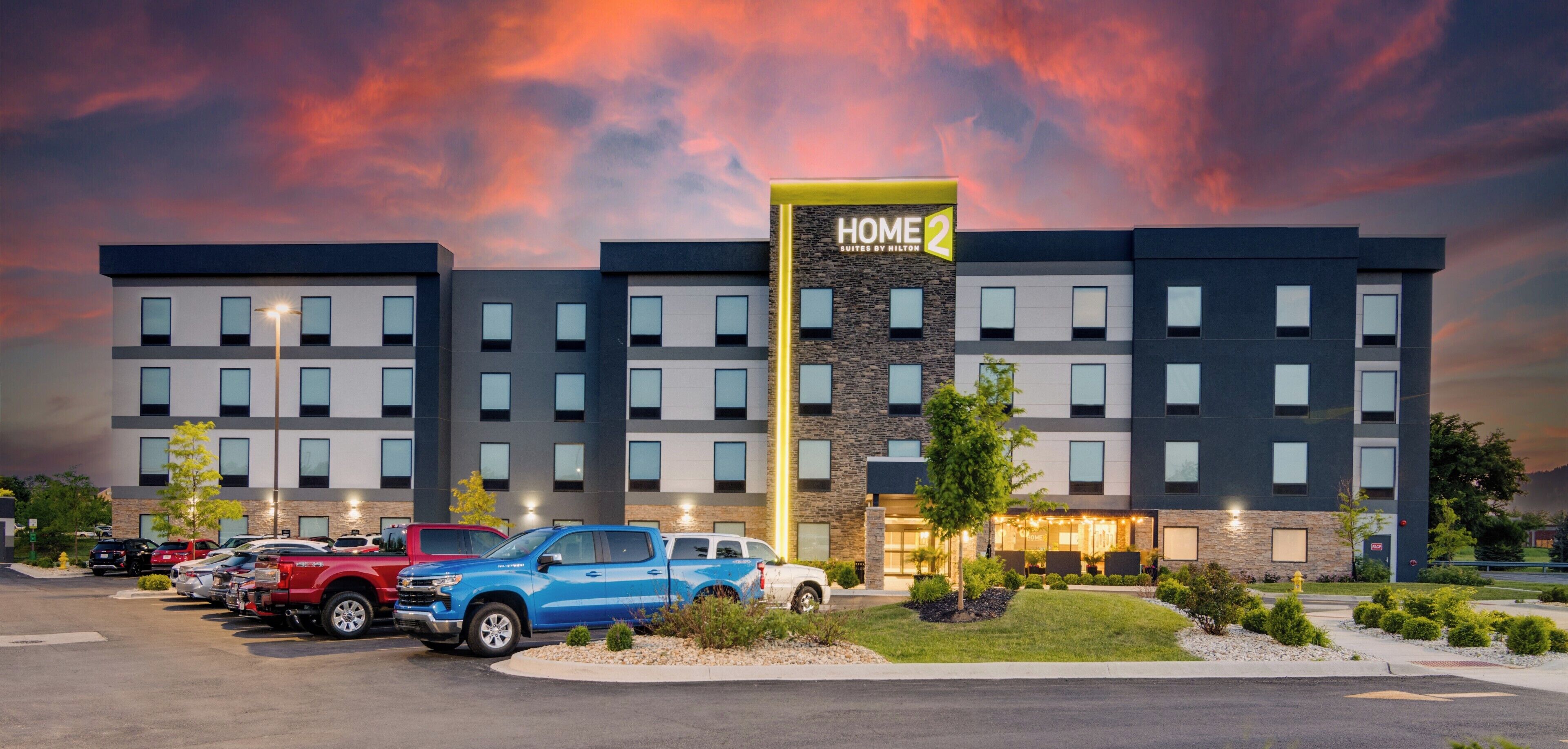 A multi-story hotel with a prominent 'HOME 2' sign, parking lot, and a well-maintained lawn.