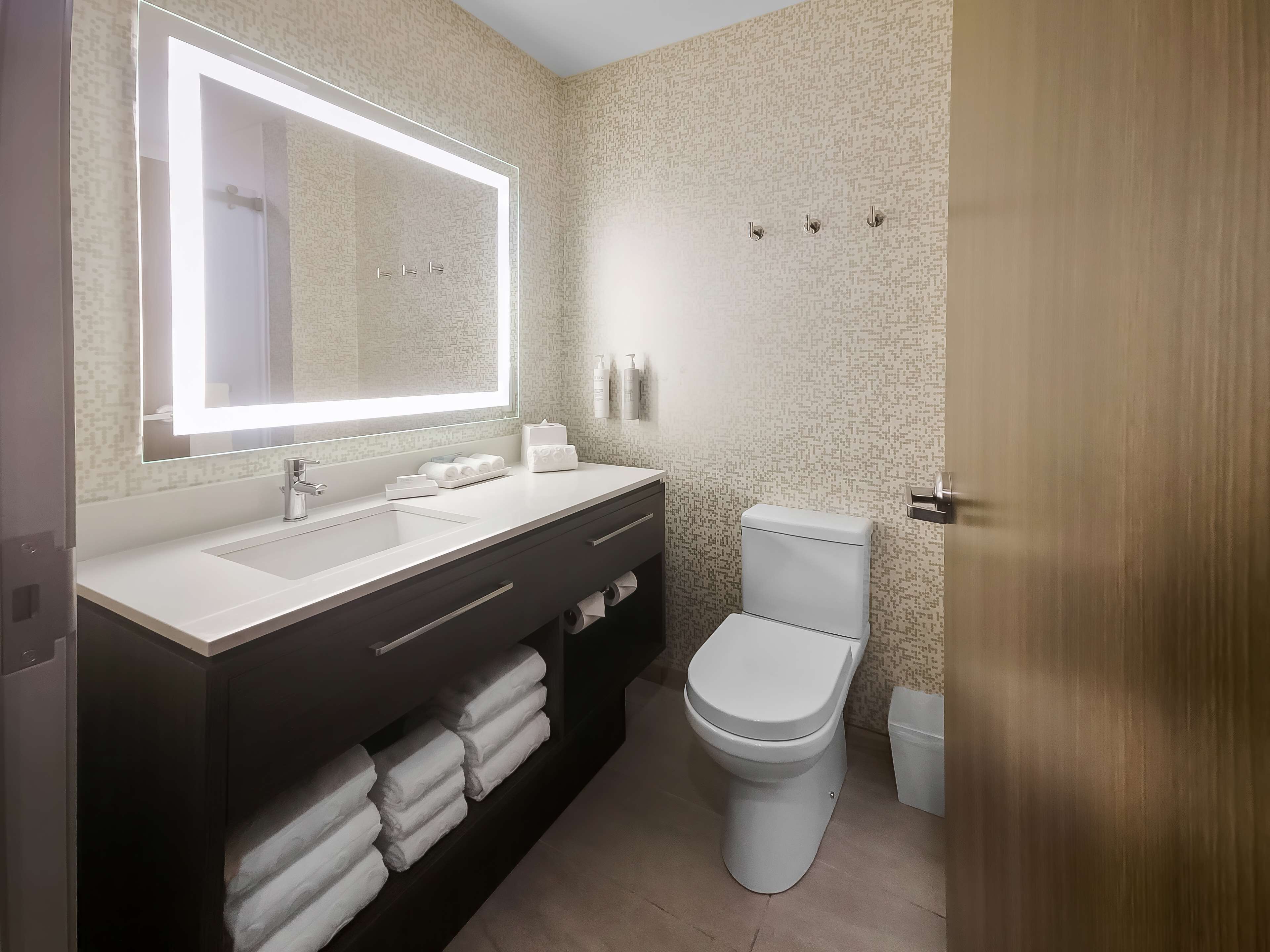 Un baño moderno con un espejo grande, lavamanos dobles, un inodoro y toallas ordenadas.