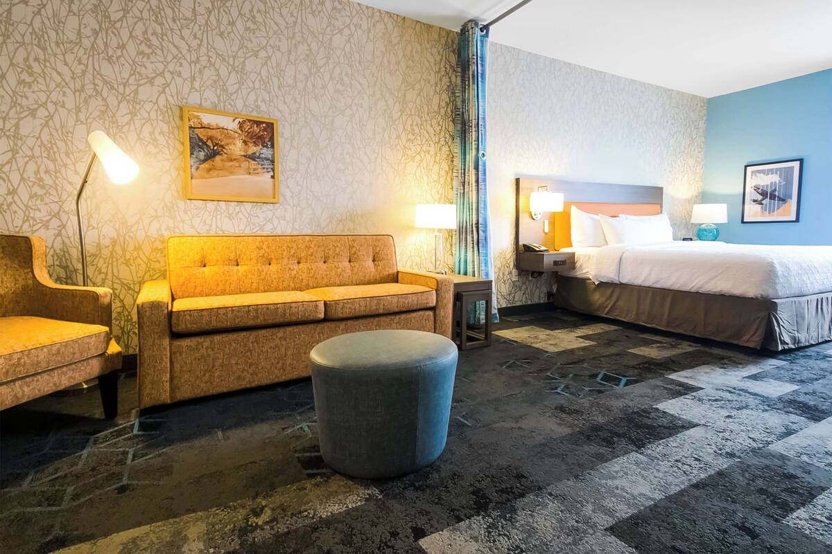 Hotellihuone, jossa on sohva, tuoli, sänky, yöpöytä ja lamppu.