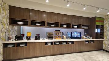Un'area cucina moderna con elettrodomestici integrati, tra cui una macchina per caffè, un forno a microonde e un frigorifero. Sono presenti scaffali con ciotole e un cartello con la scritta 'Good Morning'.