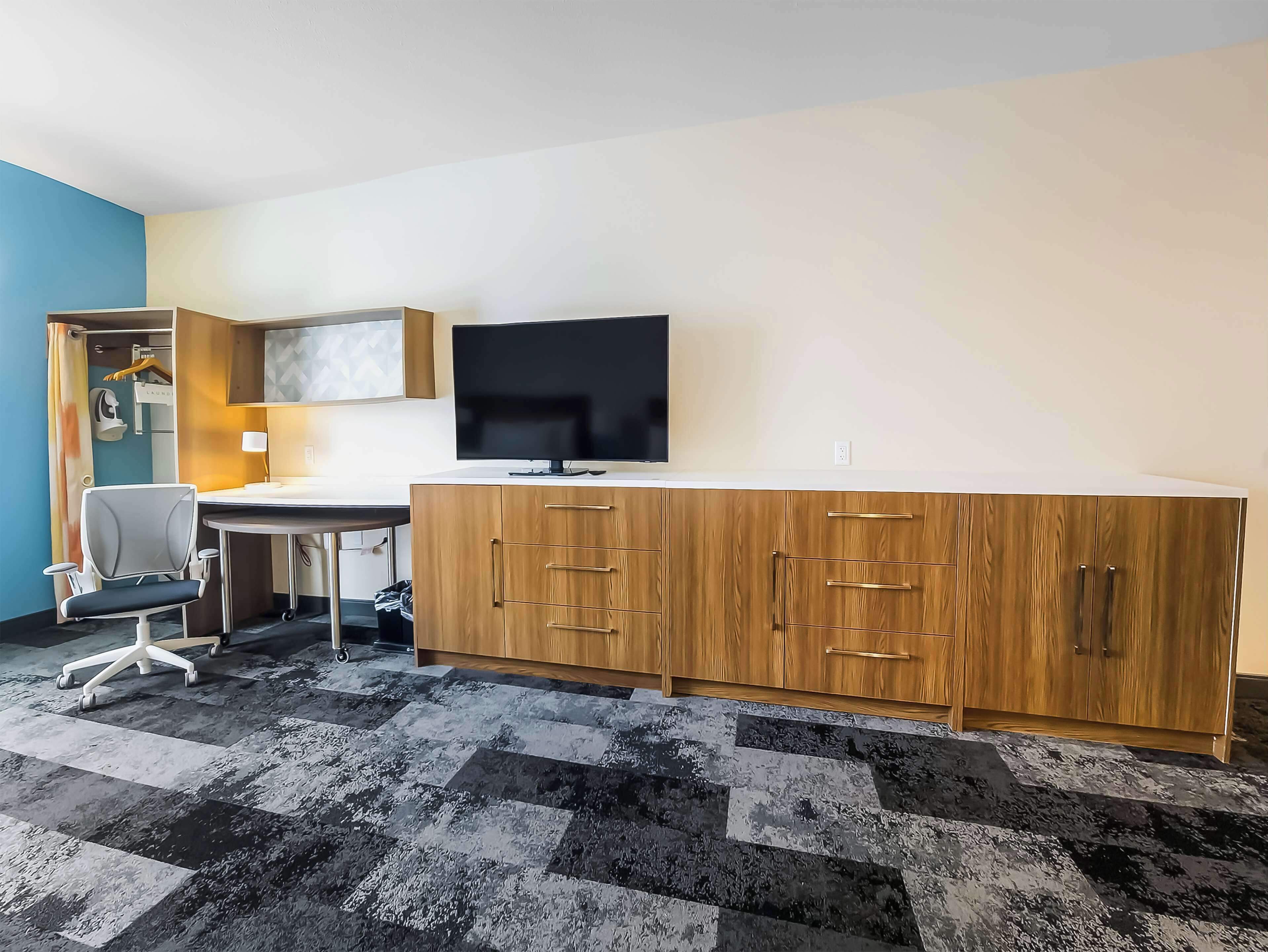 A modern room with a wooden cabinet, a desk, a chair, and a flat-screen TV.