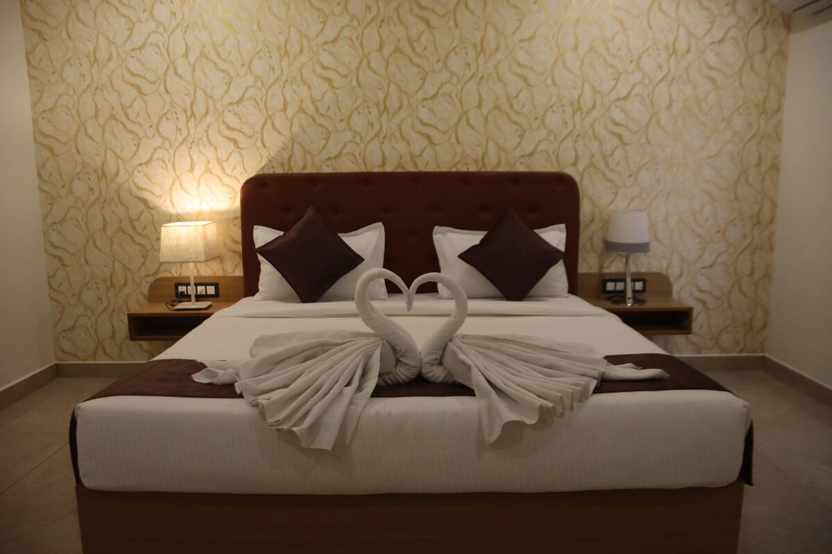 A hotel room with a bed featuring a swan-shaped towel arrangement, a wooden headboard, and patterned wallpaper.