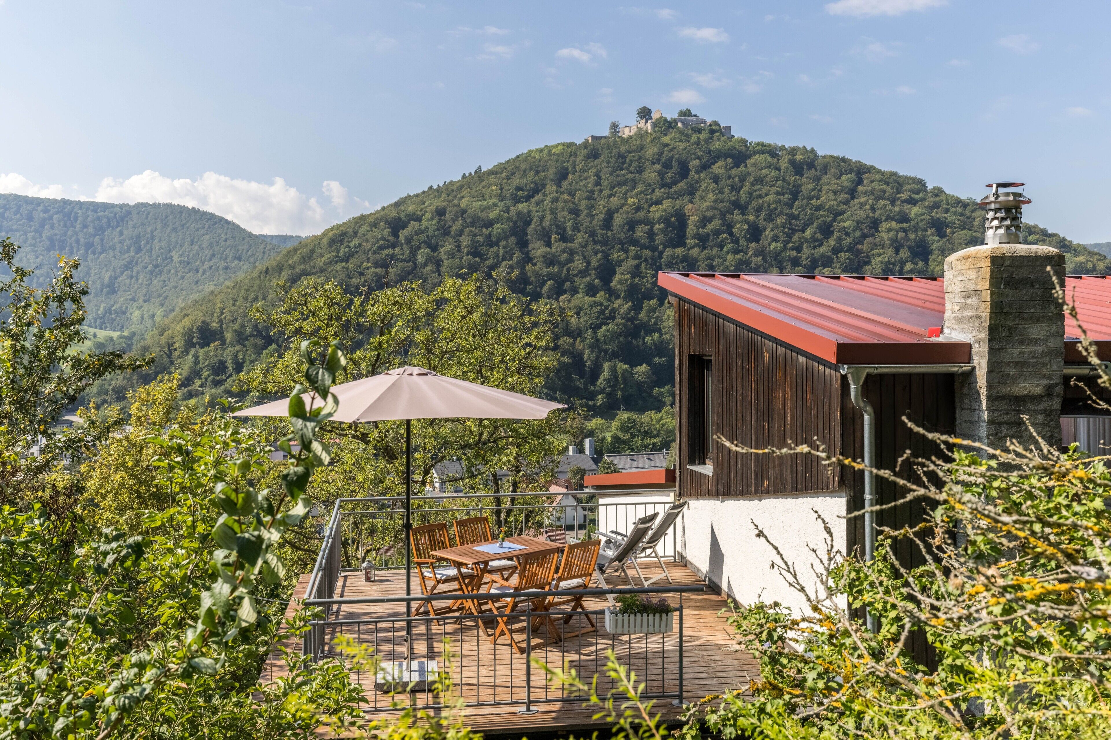 Un pontile in legno con tavolo e sedie, un edificio con tetto rosso e montagne sullo sfondo.