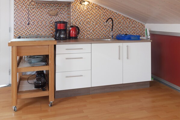 A kitchen with a tiled backsplash, a coffee maker, a kettle, and a blue dish rack.