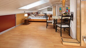 Un dormitorio estilo loft con tragaluces, suelo de madera, una cama con almohadas, un escritorio con silla y una mesa de comedor con sillas.