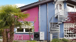 Un edificio con fachada rosa y azul, una escalera en espiral y un equipo de aire acondicionado.