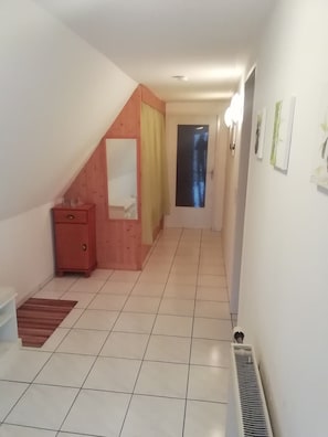 Un pasillo con techo inclinado, un aparador de madera, un radiador y una puerta con ventana.