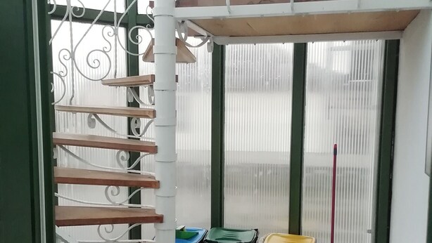 A staircase with a metal railing, a trash bin, and a broom in a room with a tiled floor. - Holiday Apartment 'Loewe' with Wi-Fi (Plau am See)