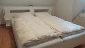A bed with white bedding and a headboard, a bedside table, and a window with curtains. - Holiday Apartment 'Loewe' with Wi-Fi (Plau am See)