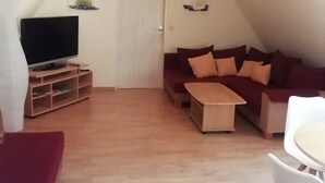 A cozy living room with a TV, a sofa, a coffee table, and a dining area with a chair. - Holiday Apartment 'Loewe' with Wi-Fi (Plau am See)