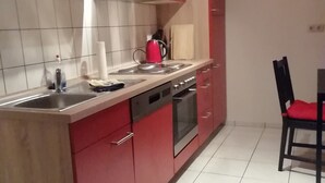 A kitchen with red cabinets, a stainless steel sink, a stove, and a dining area with a chair. - Holiday Apartment 'Loewe' with Wi-Fi (Plau am See)