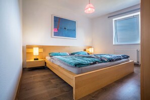 Ein Schlafzimmer mit einem hölzernen Bett, Nachttischlampen, einem Fenster und einem Gemälde an der Wand.