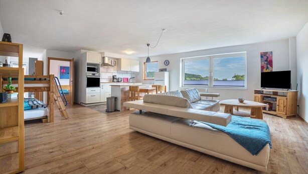 A spacious living area with a sofa, a dining table, and a kitchen in the background. - 'Knopf' Holiday Apartment with Balcony and Wi-Fi (Hardegsen)