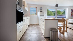 A kitchen with white cabinets, a microwave, a sink, and a window overlooking greenery. - 'Knopf' Holiday Apartment with Balcony and Wi-Fi (Hardegsen)
