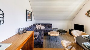 Ein gemütlicher Loft-Wohnraum mit Ecksofa, rundem Holztisch, Korbstühlen und einem Flachbildfernseher.