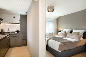 Une chambre d’hôtel moderne dotée d’un coin cuisine, d’un lit avec plusieurs oreillers et d’un lustre.