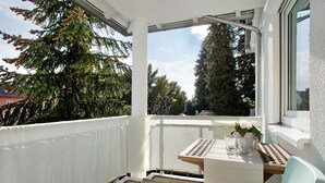 A balcony with a table and chairs, a white railing, and a view of trees and buildings.