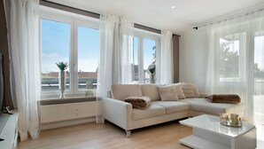 A modern living room with a sectional sofa, a coffee table, and large windows with sheer curtains.