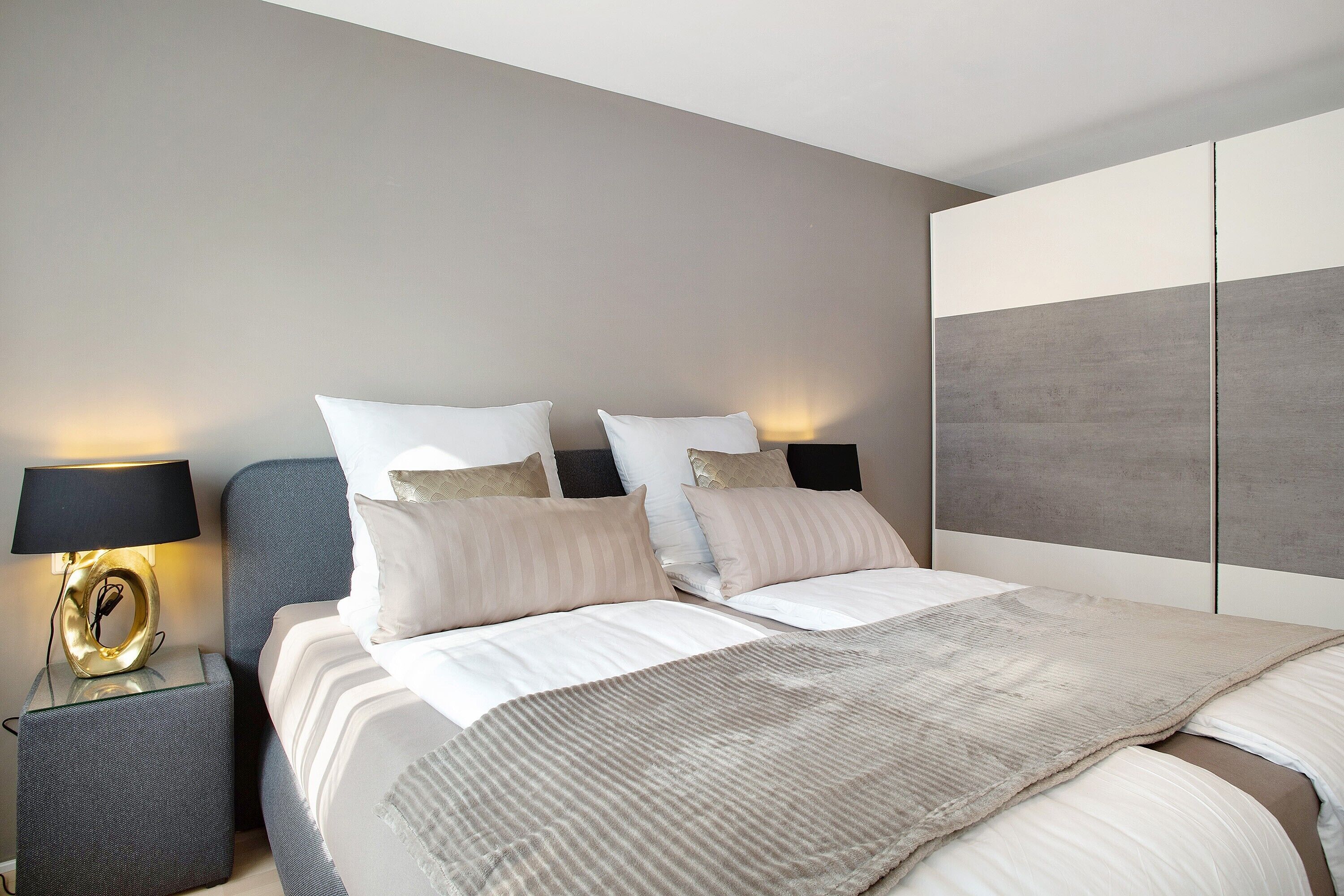 A modern bedroom with a bed, bedside tables, and a wall-mounted wardrobe.