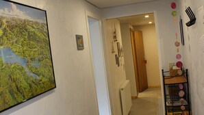 Un pasillo con un mapa, una pequeña mesa con papeles, una estantería con adornos y una puerta que da a otra habitación.