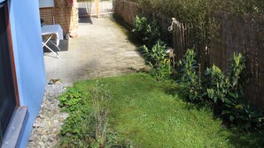 Una casa con fachada azul, una terraza de madera, un jardín cercado y un cielo despejado.