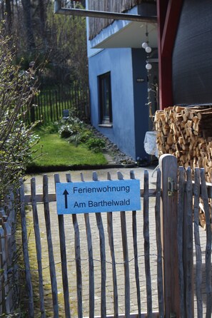 Une clôture en bois avec un panneau indicateur pointant vers « Ferienwohnung Am Barthelwald ».